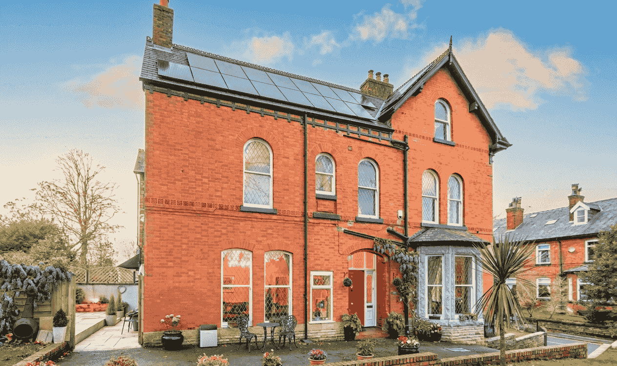 A red brick UK semi-detached home with rooftop solar panels in summer light